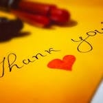 Close-up of a thank you note with a heart and pen on colored paper.